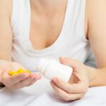 woman in her pajamas in bed holding yellow pills